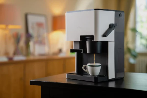 Ein NIVONA CUBE 4102 Kaffeeautomat in einem heimischen Ambiente brüht frischen Kaffee in eine weiße Espressotasse auf einem dunklen Holztisch.
