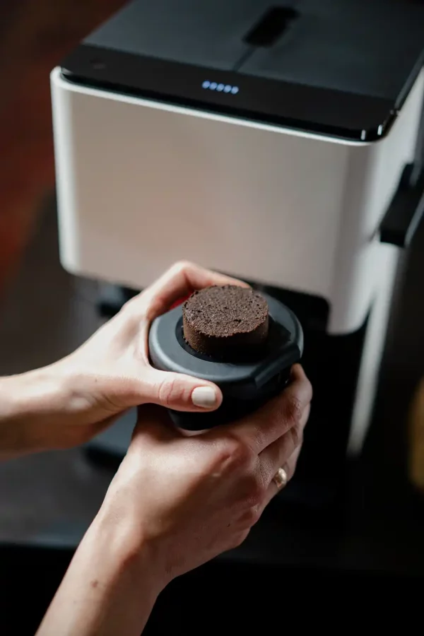 Hände, die einen kompakten Kaffeekuchen aus dem Click Cup des NIVONA CUBE 4102 Kaffeeautomaten entfernen, der eleganten Komfort und Effizienz veranschaulicht.
