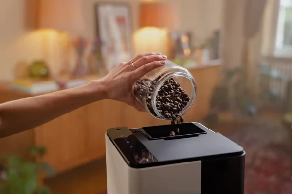 Eine Person füllt Kaffeebohnen in den Bohnenbehälter des NIVONA CUBE 4102 Kaffeeautomaten, der auf einer Küchenarbeitsplatte steht.