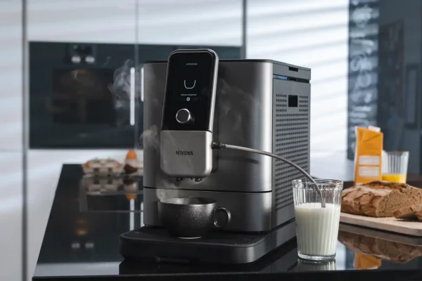 Ein NIVONA NIVO 8103 Kaffeevollautomat in Aktion, frisch gebrühter Cappuccino serviert auf einer modernen Kücheninsel mit stilvollem Interieur im Hintergrund.
